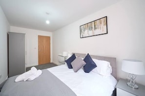 Een hotelkamer met een bed, nachtkastje, bureau, deur en een schilderij aan de muur.