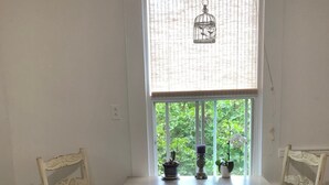 Et spiseområde med et bord og to stole, en hængende lampe og et vindue med udsigt til grøn natur.