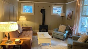 En hyggelig stue med pejs, to vinduer, en sofa, en lænestol og en lampe.