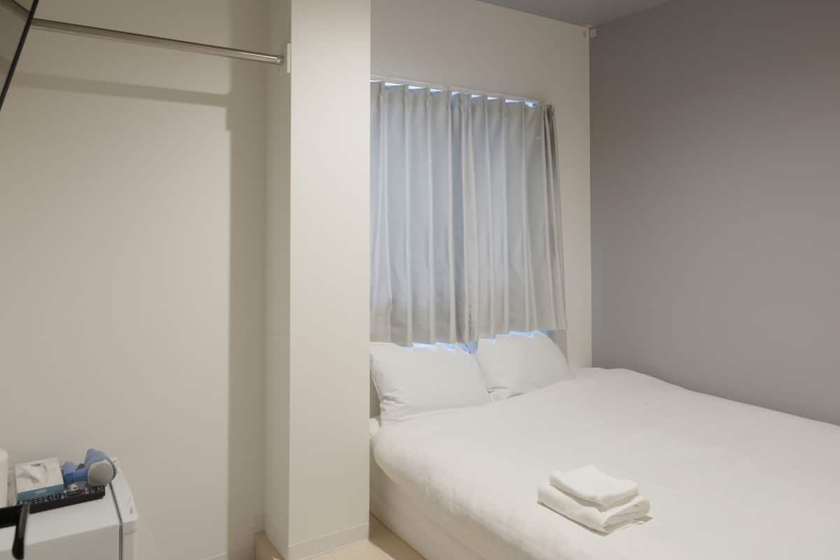 A hotel room with a single bed, a small bedside table, and a window with curtains.