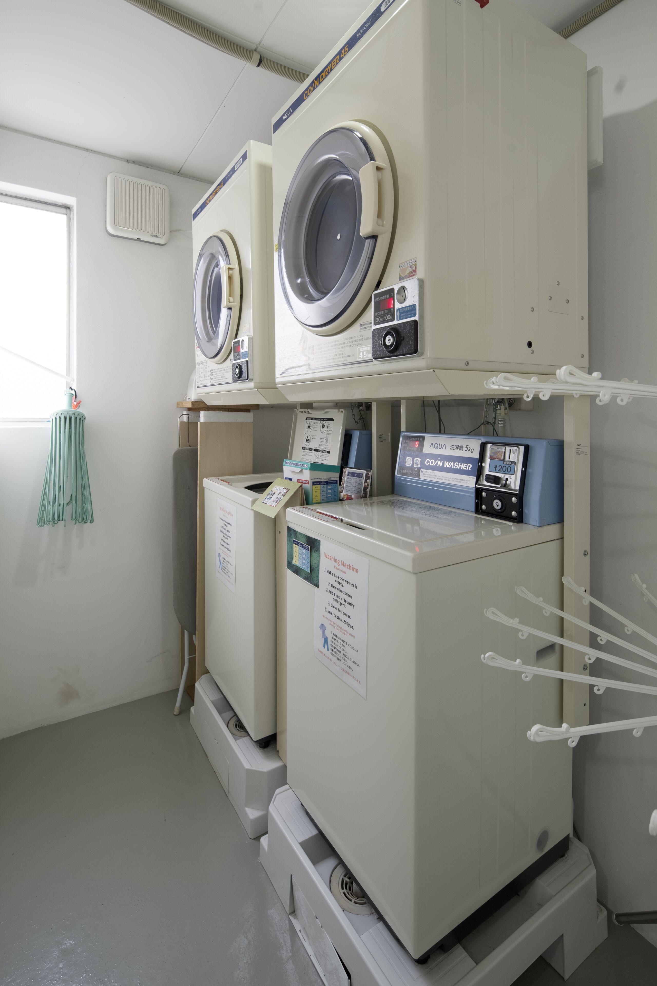 A laundry room with two large washing machines and a smaller one, equipped with control panels and a water heater.