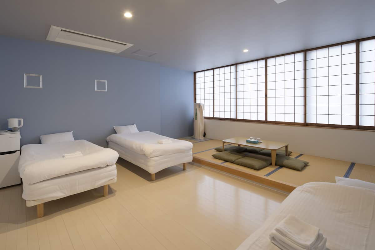 A hotel room with two beds, a small table, and a large window with a grid pattern.