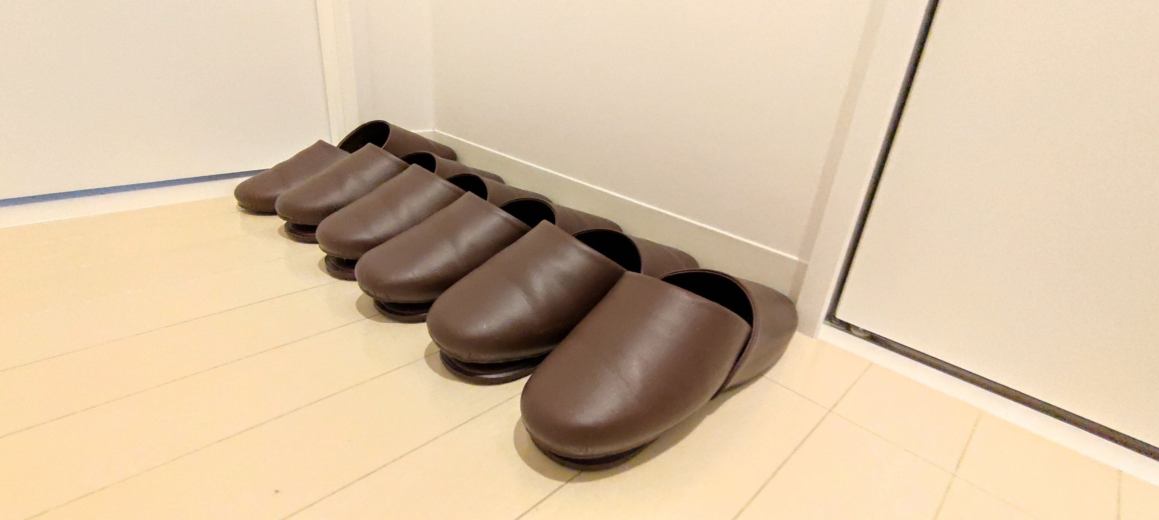 Unos zapatos marrones están alineados contra una pared en una habitación con piso de baldosas.