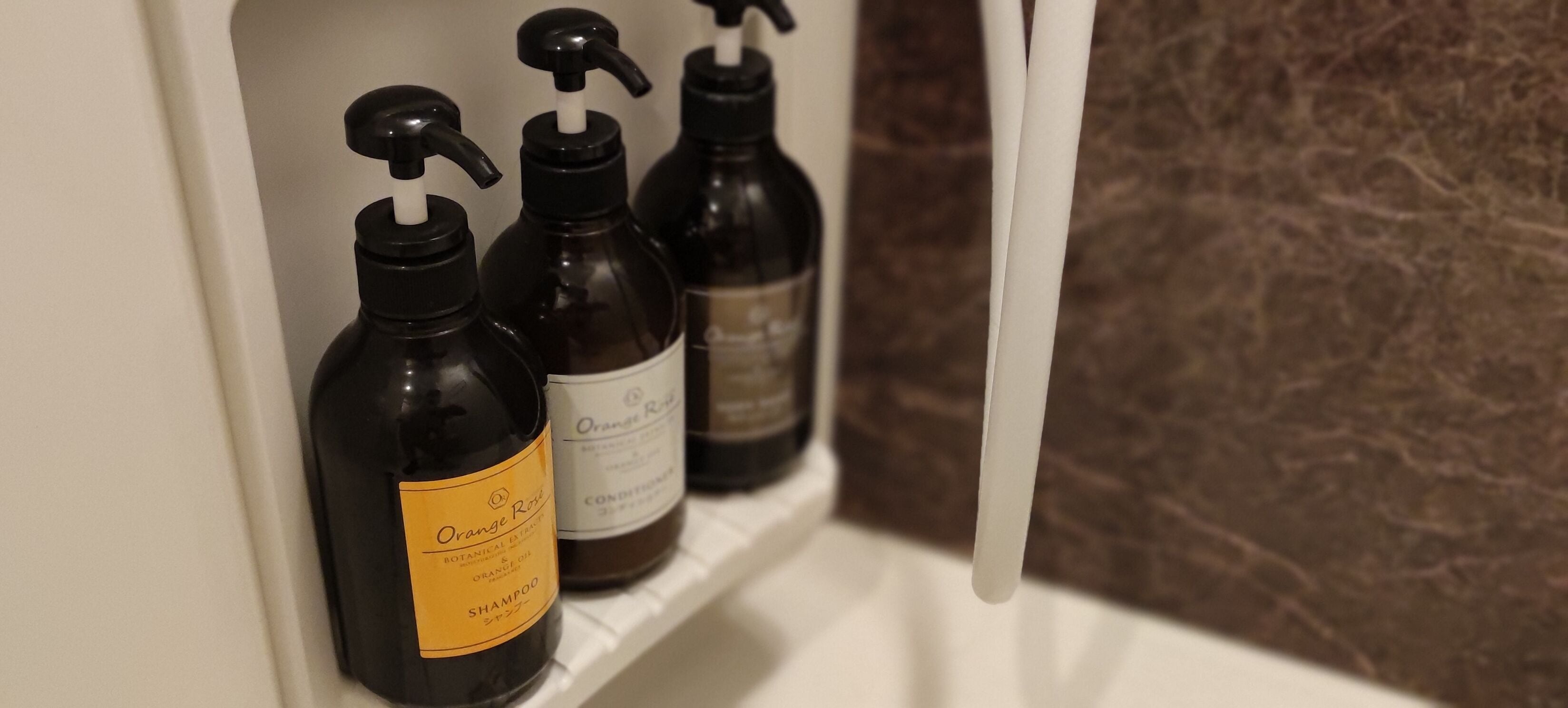 Une étagère avec trois bouteilles de lotion pour le corps au parfum d’orange.