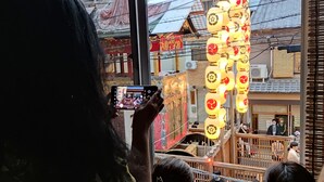 Una persona fotografiando un edificio tradicional con baranda de madera y faroles colgantes.