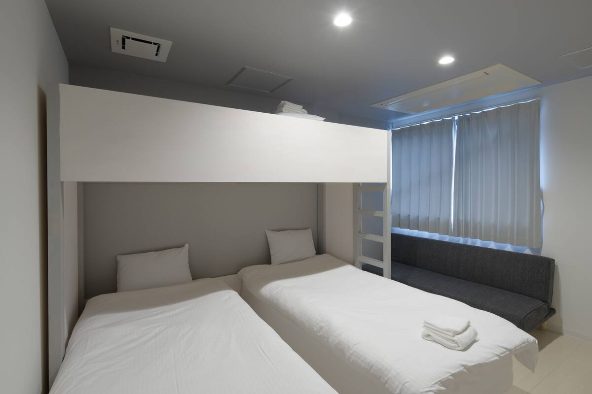 A modern bedroom with two beds, a built-in bench, and a large window with curtains.