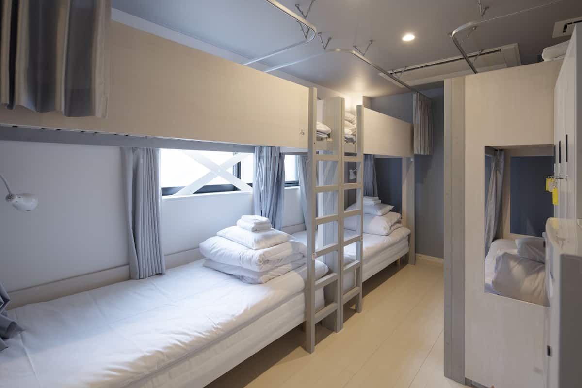 A compact hotel room with bunk beds, a ladder, a small desk, and a wardrobe.