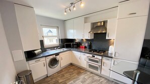 Une cuisine compacte avec des meubles blancs, un lave-linge, une cuisinière et un four à micro-ondes.
