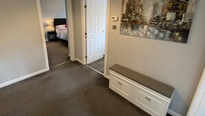 Un couloir avec un tapis gris, un banc blanc et une porte donnant sur une chambre à coucher.