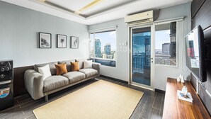 A modern living room with a sofa, a coffee table, and a large window offering a city view. - PECAN by Kozystay (Jakarta)