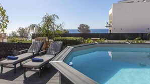 Ein Swimmingpool mit Liegestühlen und Blick aufs Meer.