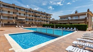 Una piscina con sillas de descanso y un edificio de varios pisos con balcones.