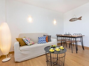 Un salon accueillant avec un canapé, une table basse ronde sur laquelle sont posées des tasses jaunes, une table à manger avec des chaises et une décoration murale représentant des poissons.