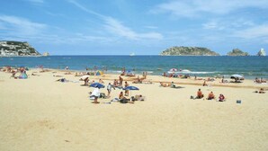 Una playa con gente tomando el sol y nadando, tiendas de campaña y sombrillas.