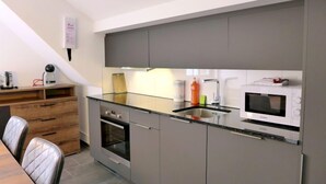 A compact kitchen with grey cabinets, a stainless steel sink, a microwave, and a small oven. - Henry's 300 by Interhome (Interlaken)