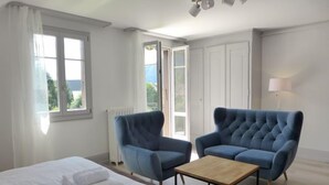 A bedroom with a bed, two blue armchairs, a wooden coffee table, a window with curtains, a radiator, and a lamp. - Henry's 300 by Interhome (Interlaken)