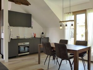 A modern kitchen with dark cabinets, a built-in oven, and a dining area with a wooden table and four chairs.
