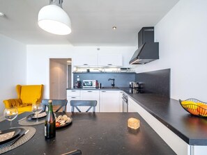 A modern kitchen with white cabinets, a black countertop, and a yellow chair. - Résidence Les Trois Iles by Interhome (Quiberon)