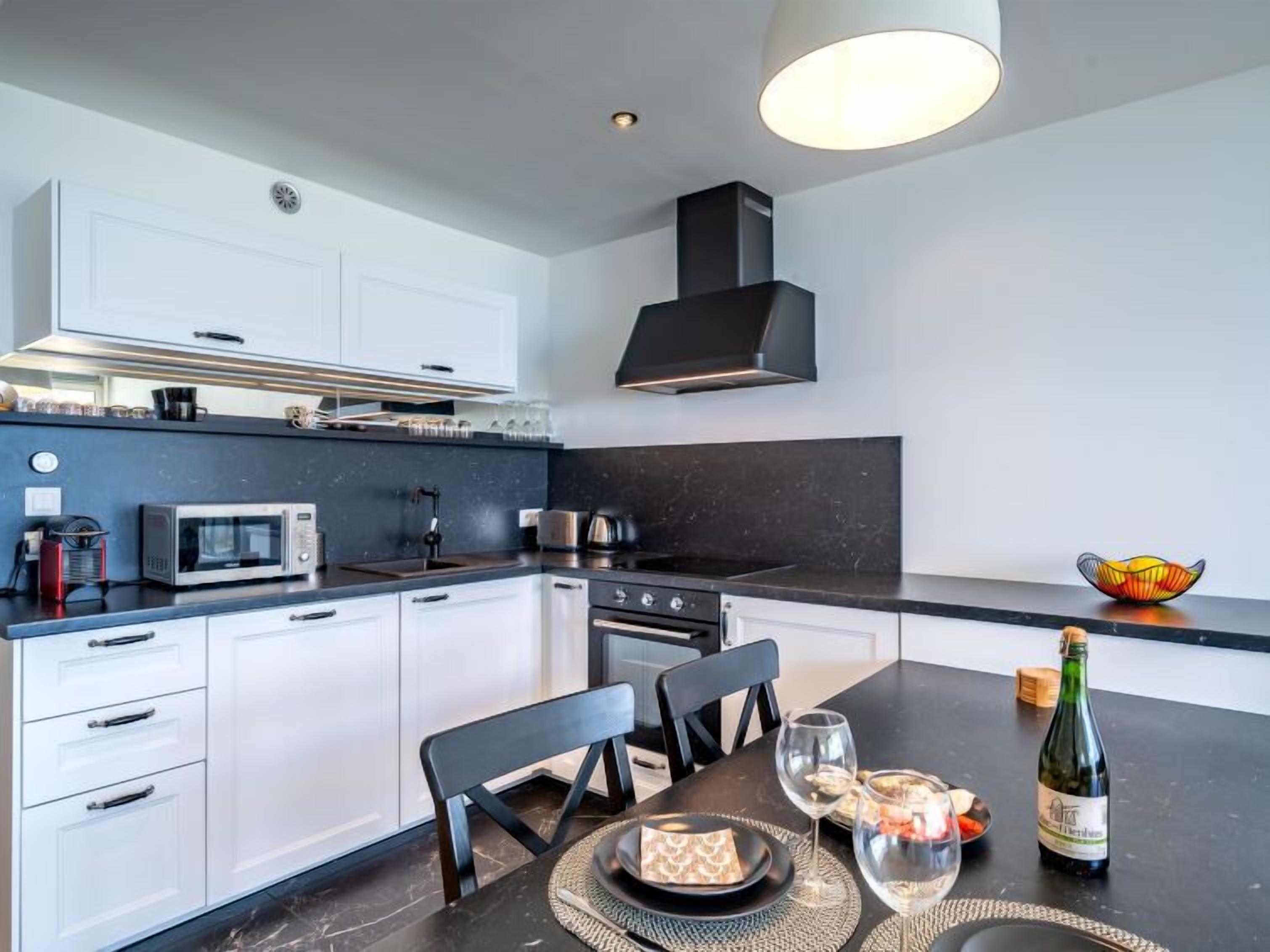 A modern kitchen with white cabinets, a black countertop, a stove, and a dining area with a table set for two.