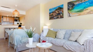 Ein modernes Wohnzimmer mit einer Couch, einem kleinen runden Tisch mit einer Fruchtschale und einem Glas, sowie einer Topfpflanze.