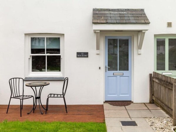 Un bâtiment blanc avec une porte bleue, une petite table avec deux chaises et une enseigne sur laquelle on peut lire « SEA ECHO ».