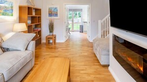A living room with a sofa, a TV, a fireplace, and a bookshelf. - Sea Echo by Interhome (Charlestown)