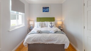 A neatly made bed with white linens, a green headboard, and matching pillows. There are two bedside tables with lamps and a framed picture above the bed. - Sea Echo by Interhome (Charlestown)