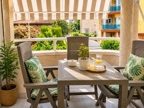 A covered outdoor seating area with wicker furniture, a table with a pitcher and glasses, and a view of a garden and buildings. - Beautiful And Bright Apartment In Calafell, (Calafell)