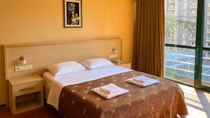 A hotel room with a large bed, two bedside tables, a nightstand, a framed picture on the wall, and a window with a view of buildings. - Batesta Hotel (Tbilisi)