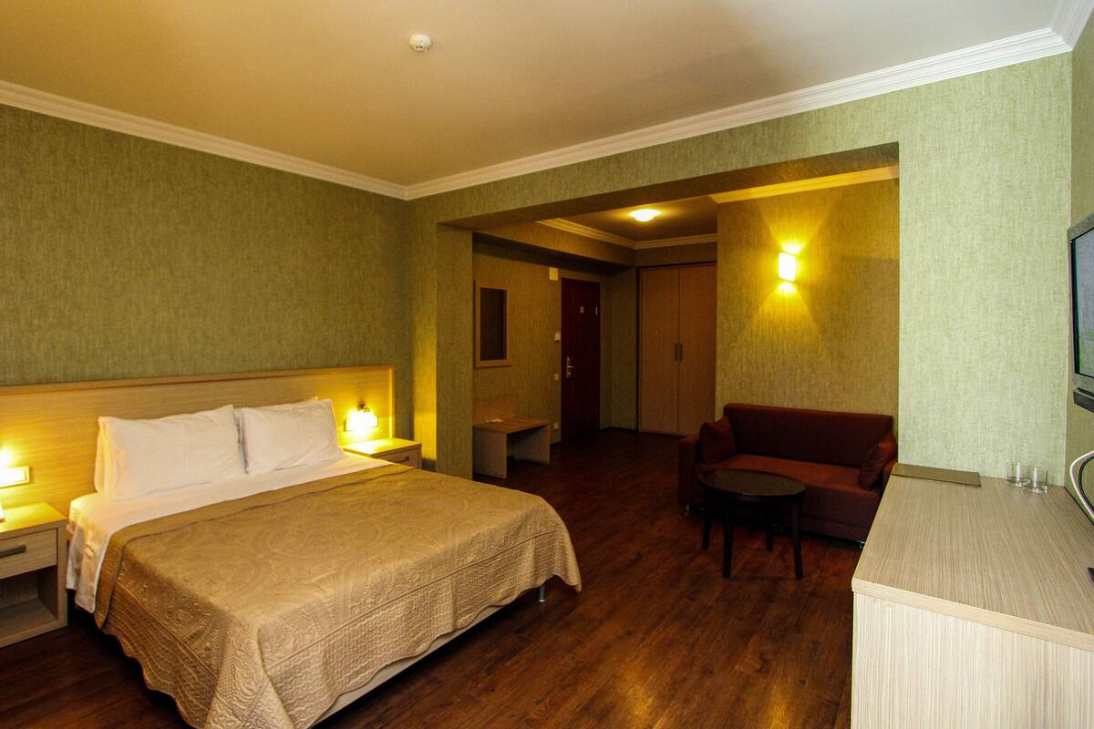A hotel room with a bed, bedside table, lamp, and a small seating area with a table and chair.