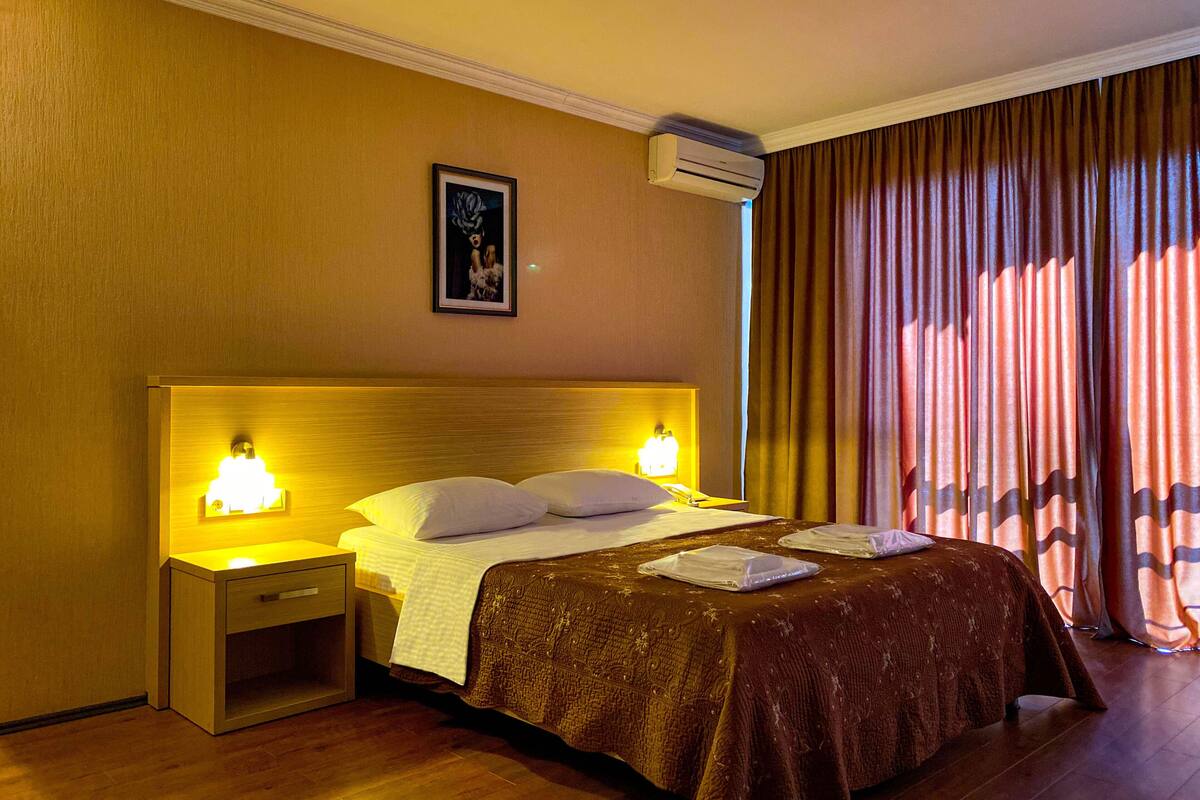 A hotel room with a bed, bedside lamps, a framed picture on the wall, and a window with curtains.