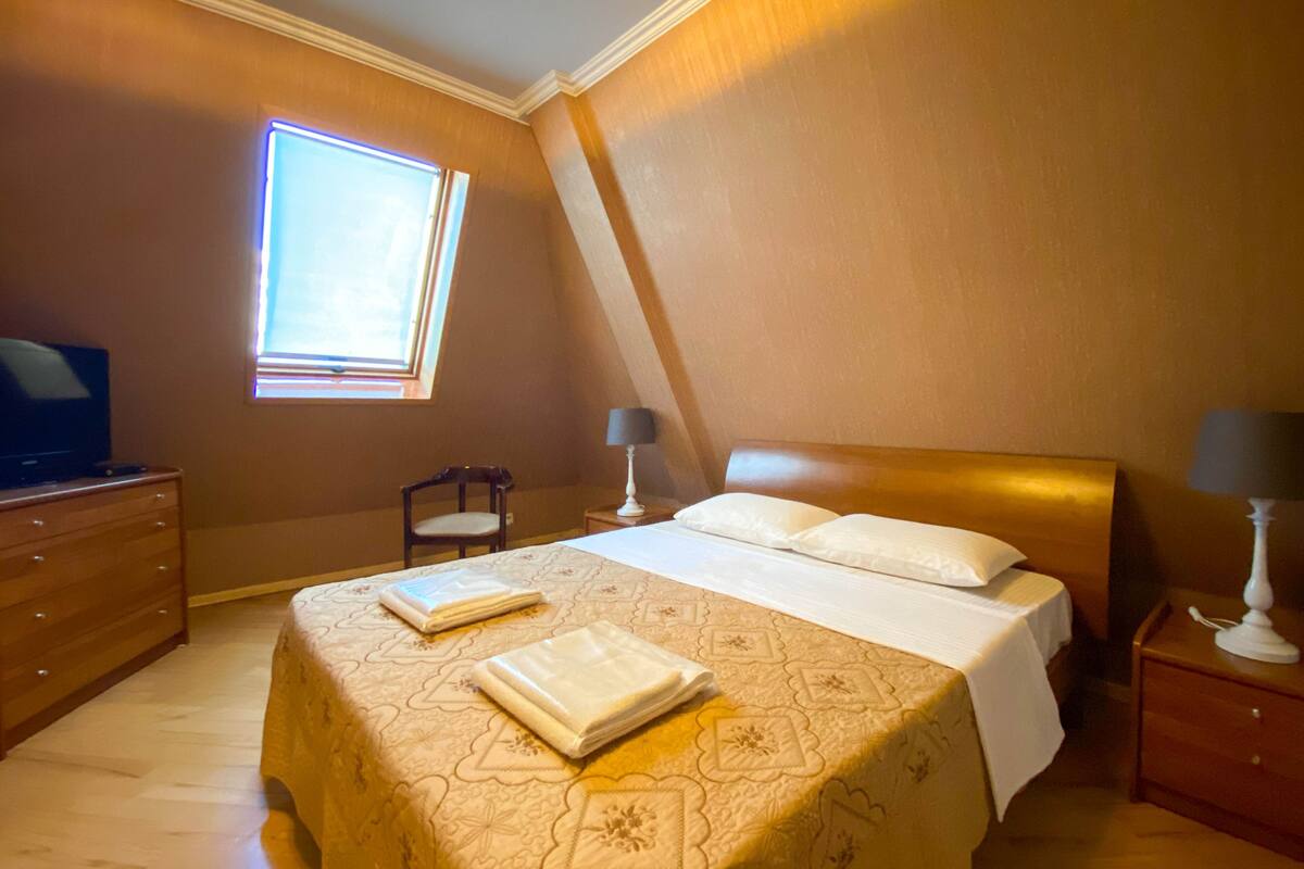 A bedroom with a bed, a dresser, a chair, a nightstand, a lamp, and a window.