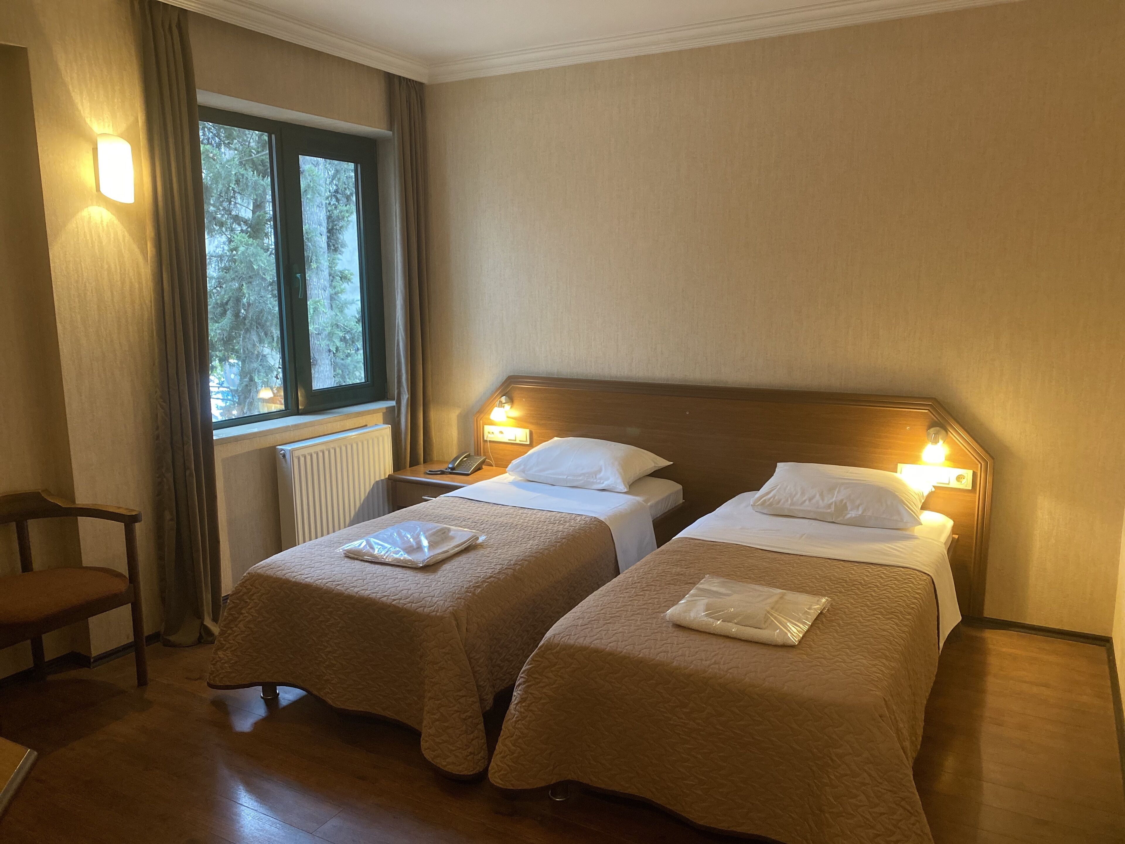 Habitación de hotel con dos camas, una silla, una ventana con cortinas y un radiador.