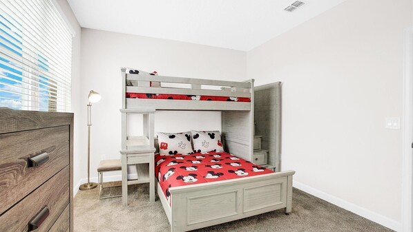 A bunk bed with a red Mickey Mouse themed bedspread, a bedside table, and a lamp.