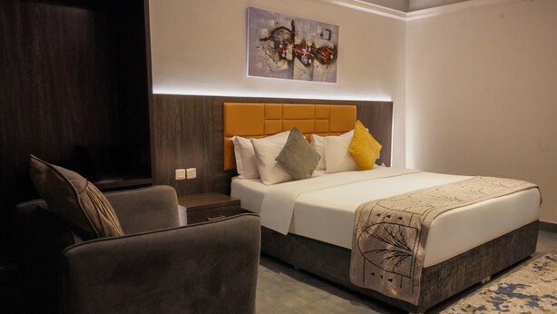 A modern hotel room with a large bed, a seating area, and a wall-mounted artwork. - Tura Residence Qurtuba (Riyadh)