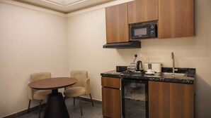 A compact kitchen with a microwave, coffee maker, and dishwasher. There is a small dining table with two chairs. - Tura Residence Qurtuba (Riyadh)