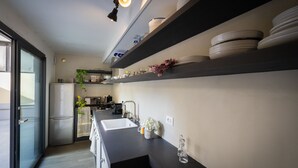 Una cocina moderna con encimera negra, electrodomésticos de acero inoxidable y repisas blancas con vajilla.