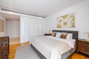 A bedroom with a bed, a nightstand, a dresser, a painting, and a door.