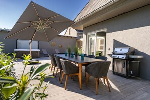 Une terrasse extérieure avec une table, des chaises, un barbecue et un parasol.