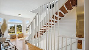 A modern staircase with white railings and wooden steps, leading to a landing with a glass table and chairs. - 1525 - Pampa Hill - Poolside Corolla Getaway w/ Theater Room (Corolla)