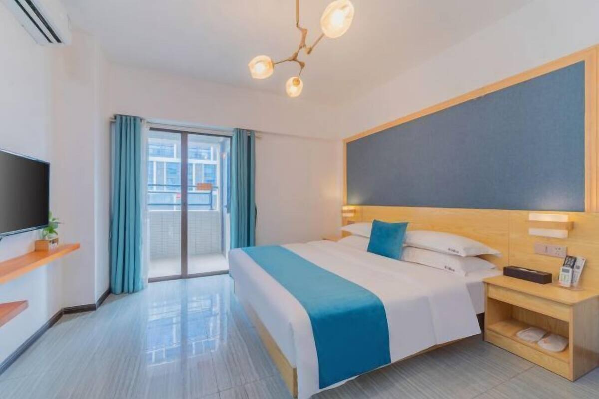 Una habitación de hotel moderna con una cama grande, un televisor de pantalla plana, una mesita de noche de madera y vistas a la ciudad a través de la ventana.