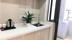 A kitchen with a white countertop, a sink, a potted plant, a kettle, and a coffee machine. - Feilisi Apartment (Zhongshan Yuelai South Road) (Zhongshan)