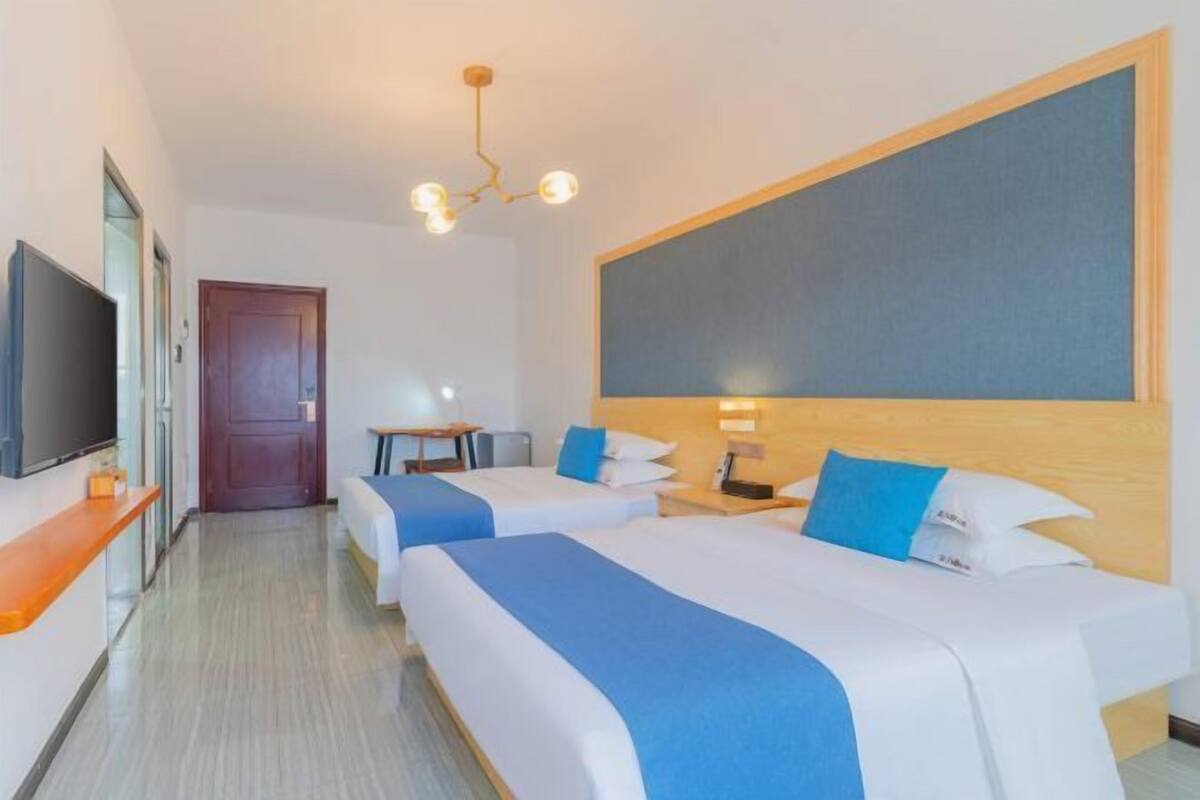 Habitación de hotel con dos camas, un escritorio, un televisor y un ventanal grande.