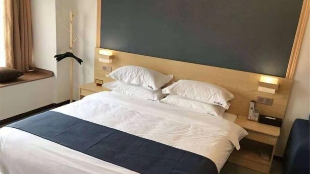 A hotel room with a large bed, bedside tables, a wall-mounted TV, and a window with curtains. - Feilisi Apartment (Zhongshan Yuelai South Road) (Zhongshan)