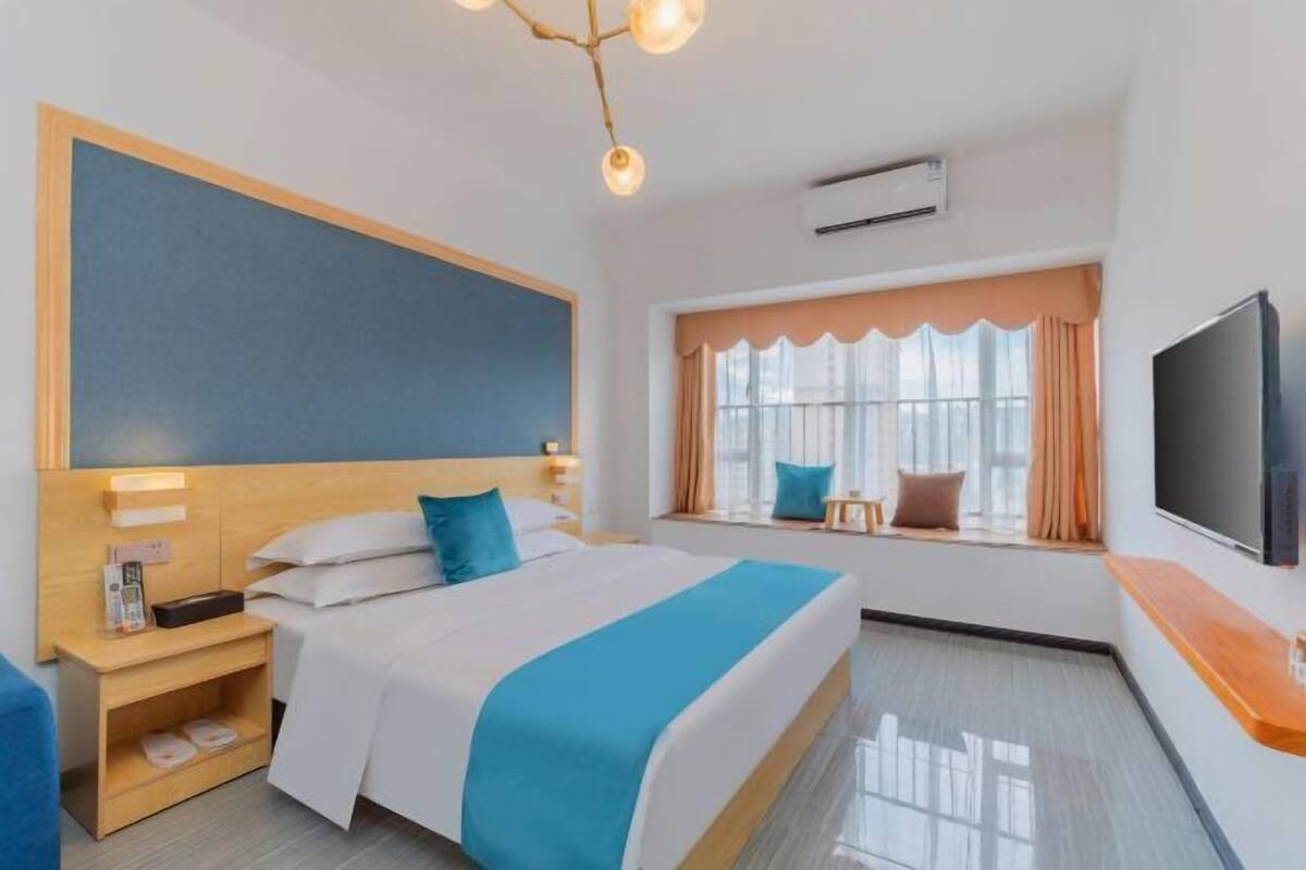 Habitación de hotel con cama, mesita de noche, televisión, ventana con cortinas e iluminación en el techo.