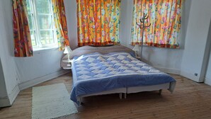 Une chambre avec un plancher en bois, un lit recouvert d’une couette bleue, des rideaux à motifs floraux et une lampe de chevet.