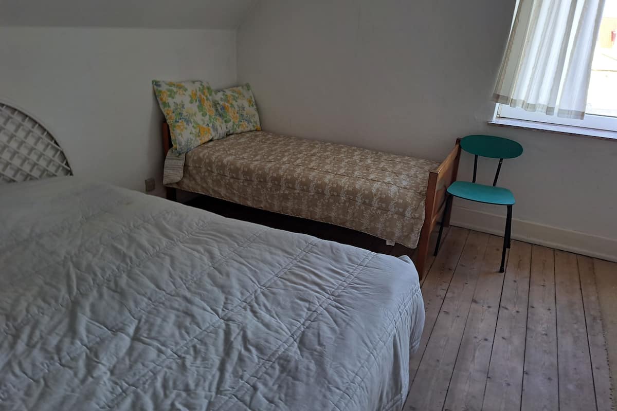 A bedroom with two beds, a window with curtains, and a wooden floor.