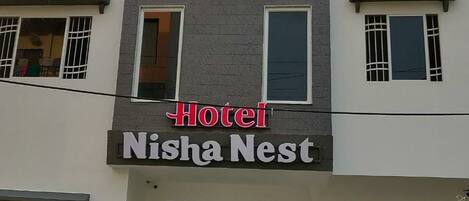 Hotel Nisha Nest met een modern gevelontwerp, inclusief een opvallende rode boog boven de ingang en een bord met de naam van het hotel.