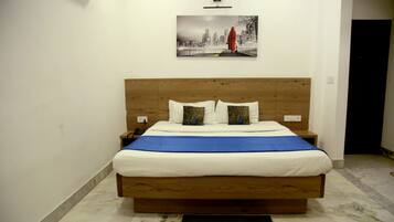 A hotel room with a wooden bed, white bedding, and a cityscape painting on the wall.