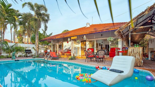 A swimming pool with a lounge chair and colorful balls, surrounded by palm trees and a building with a tiled roof. - Exclusive Villa, 6 Bedrooms, Private Pool, Garden View, 10 Mins LK Metro (Pattaya)